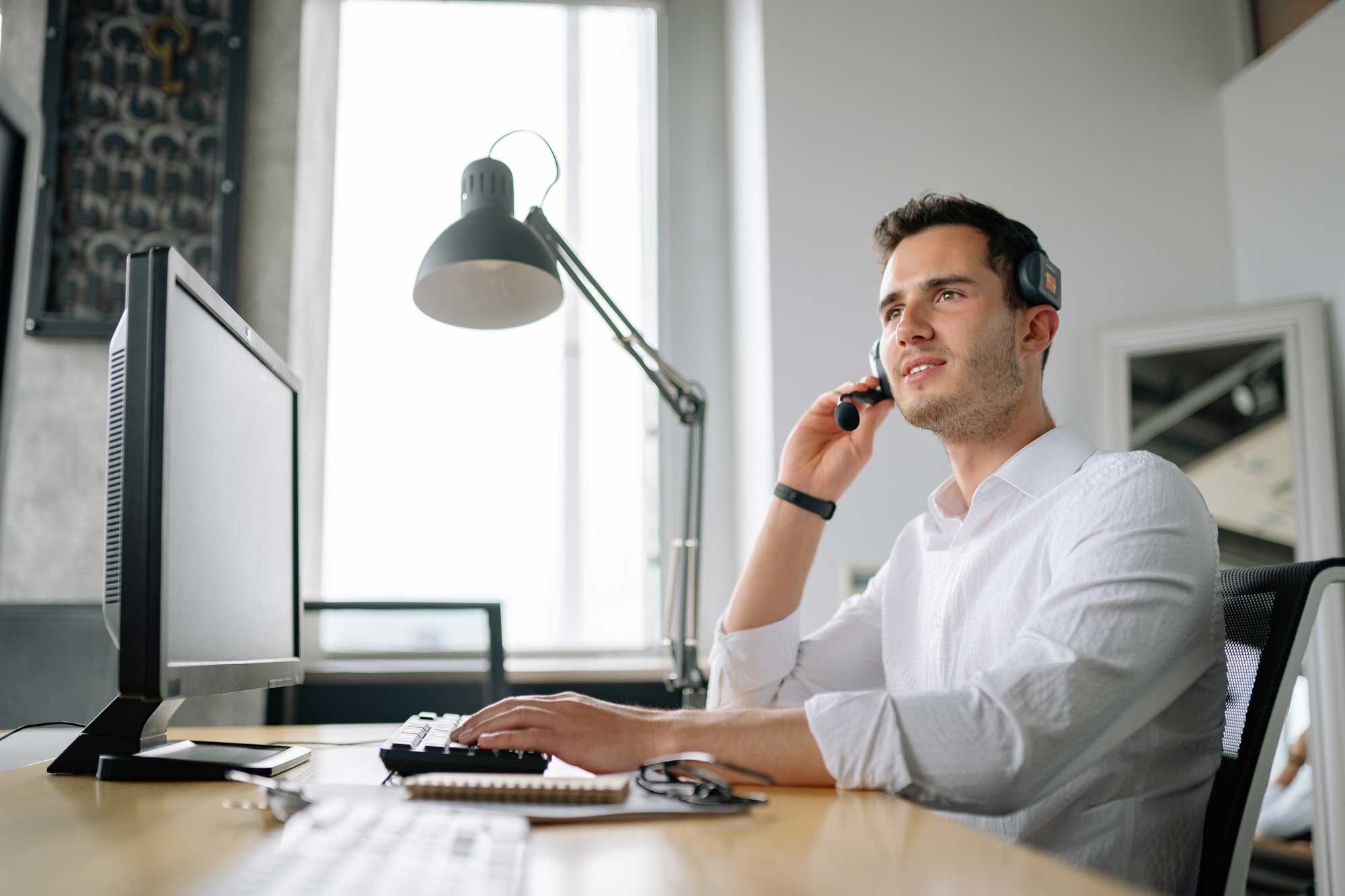 service_web Kundenberater sitzt am Laptop und telefoniert via Headset
